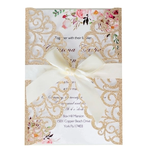 Detail of laser-cut gold glitter wedding invitation sleeve with silk ribbon and floral insert