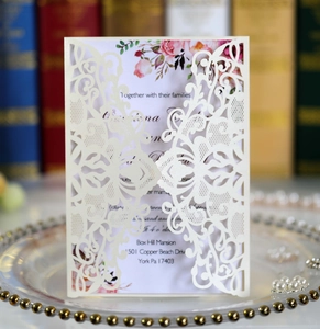Macro detail of laser-cut lace pattern on white wedding invitation card with floral insert