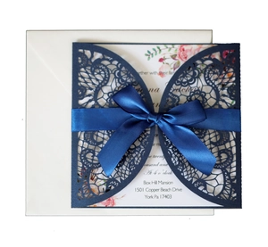 Detail of laser-cut lace wedding invitation with navy ribbon and floral insert card