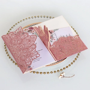 Dettaglio dell'invito di nozze glitter oro rosa con intricato motivo floreale a taglio laser