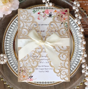 Detail of laser-cut wedding invitation with gold glitter cover and satin bow on a plate