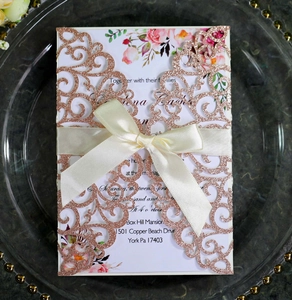 Macro detail of laser cut glitter invitation with elegant rose gold vine patterns and ribbon