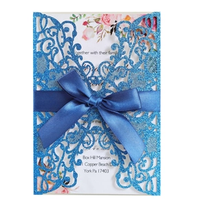 Macro detail of laser-cut glitter wedding invitation with blue velvet ribbon and floral inlay