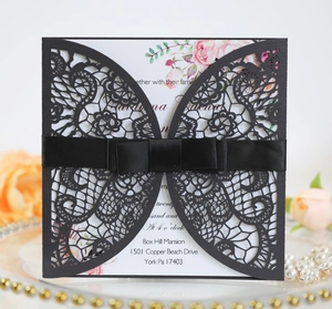 Macro detail of laser-cut black lace invitation with silk ribbon and floral insert