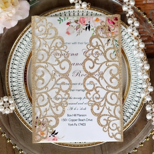Close-up of laser-cut gold glitter wedding invitation with floral insert and ornate details