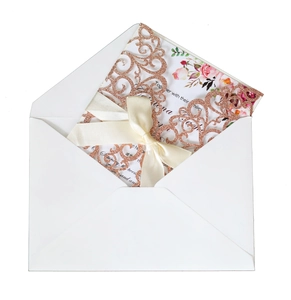 Detail of laser-cut glitter wedding invitation with rose gold floral pattern and silk bow