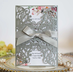 Detail of silver laser-cut wedding invitation with intricate vine patterns and grey ribbon