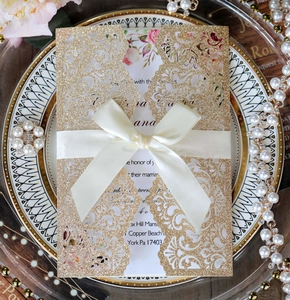 Detailed laser cut gold glitter wedding invitation featuring elegant ribbon and floral insert