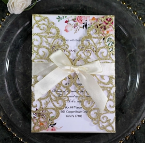 Close-up of laser-cut glitter wedding invitation with elegant satin bow on a glass tray