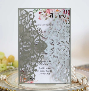 Macro shot of silver laser-cut floral invitation cover on an elegant gold-rimmed plate