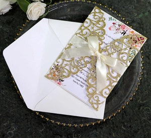 Detailed laser-cut gold glitter wedding invitation with white satin bow and envelope