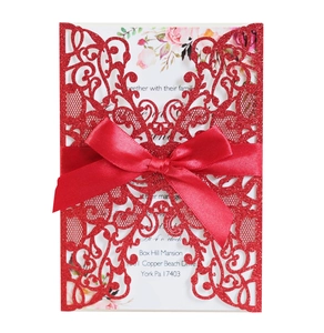 Detail of red glitter laser cut wedding invitation with silk bow and floral insert