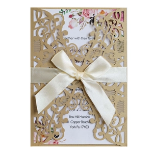 Macro detail of laser-cut gold lace invitation cover with elegant white silk ribbon