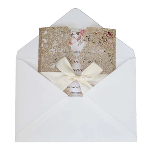 Detailed laser cut gold glitter wedding invitation with white satin bow and floral inner card
