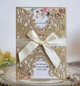 Detail of laser cut wedding invitation with cream silk bow and floral printed insert