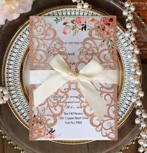 Macro detail of laser-cut rose gold glitter wedding invitation with beige satin bow