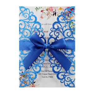 Macro detail of laser cut glitter wedding invitation with blue satin ribbon and floral card
