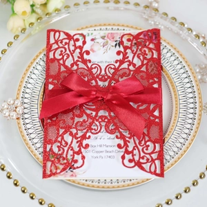 Detailed close-up of red laser-cut glitter wedding invitation with silk bow and inner card