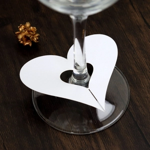 Close-up of elegant white heart-shaped hollow paper place cards on wine glass stems