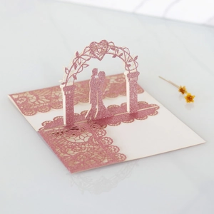 Macro detail of laser-cut 3D wedding card with pink glitter and floral arch silhouettes