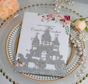 Close-up of laser-cut silver glitter castle and carriage wedding invitation card set