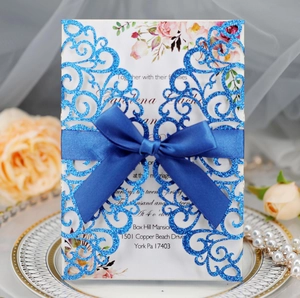 Close-up of blue glitter laser-cut wedding invitation with a navy ribbon and floral details