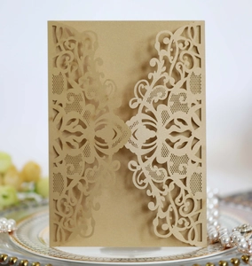 Macro detail of laser-cut champagne gold lace invitation with elegant floral vine patterns
