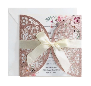 Detailed laser-cut floral texture on rose gold glitter wedding invitation with silk bow