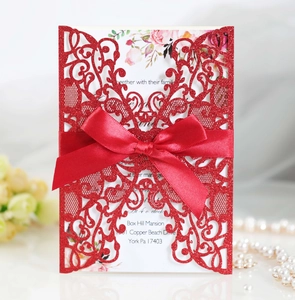 Close-up of red laser-cut lace invitation card with glitter texture and satin bow