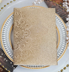 Dettaglio dell'invito di nozze dorato glitterato con intricati motivi floreali mandala