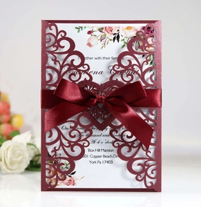Close-up of laser-cut burgundy wedding card with satin ribbon and floral insert