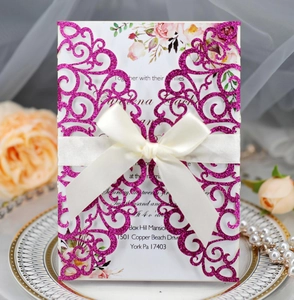 Detail of laser-cut glitter invitation with floral inner card and white satin ribbon bow