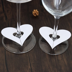 Close-up of white heart-shaped paper place cards placed on wine glass stems for weddings