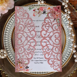 Macro view of laser-cut rose gold glitter wedding invitation with floral inner card