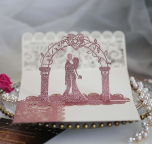 Macro detail of 3D pop-up wedding card showing a couple under a glittery rose gold arch