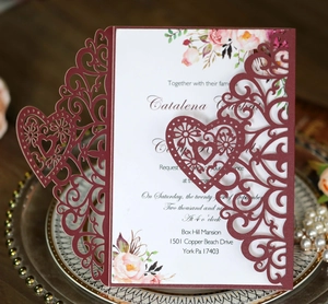 Detail of laser-cut burgundy lace wedding invitation with floral inner card on porcelain