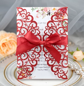 Macro shot of red glitter laser-cut wedding invitation with elegant satin bow on a plate
