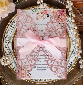 Detail of laser-cut pink glitter wedding invitation with satin bow on a decorative plate