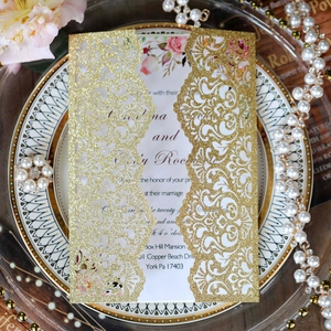 Close-up of laser-cut gold glitter wedding invitation with elegant floral scroll patterns