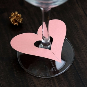 Detailed view of pink heart-shaped laser-cut place card on a wine glass stem for weddings