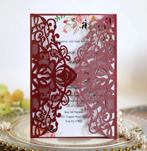 Detail of laser-cut burgundy wedding invitation with elegant floral insert and pearl accents