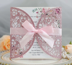 Detail of pink glitter laser-cut wedding invitation with elegant satin ribbon bow