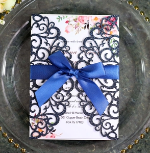 Detail of laser-cut glitter wedding invitation with royal blue ribbon and floral inner card