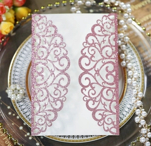 Detailed laser-cut hollow pink glitter invitation card with ribbon on bone china plate