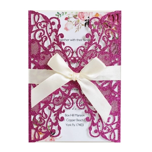 Detail of laser-cut glitter wedding invitation with satin bow and floral inner card