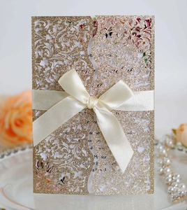 Detail of laser-cut wedding invitation with gold glitter texture and ivory satin ribbon