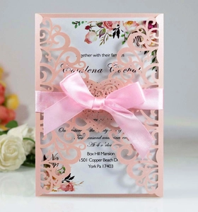 Detail of pink laser-cut wedding invitation with elegant floral patterns and silk bow