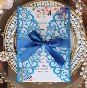 Detail of laser-cut wedding invitation with blue glitter finish and satin ribbon bow