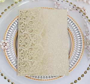 Detail of laser-cut champagne gold glitter paper wedding invitation with floral patterns