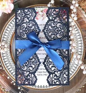 Detail of laser-cut glitter navy blue invitation with elegant satin bow and floral inner